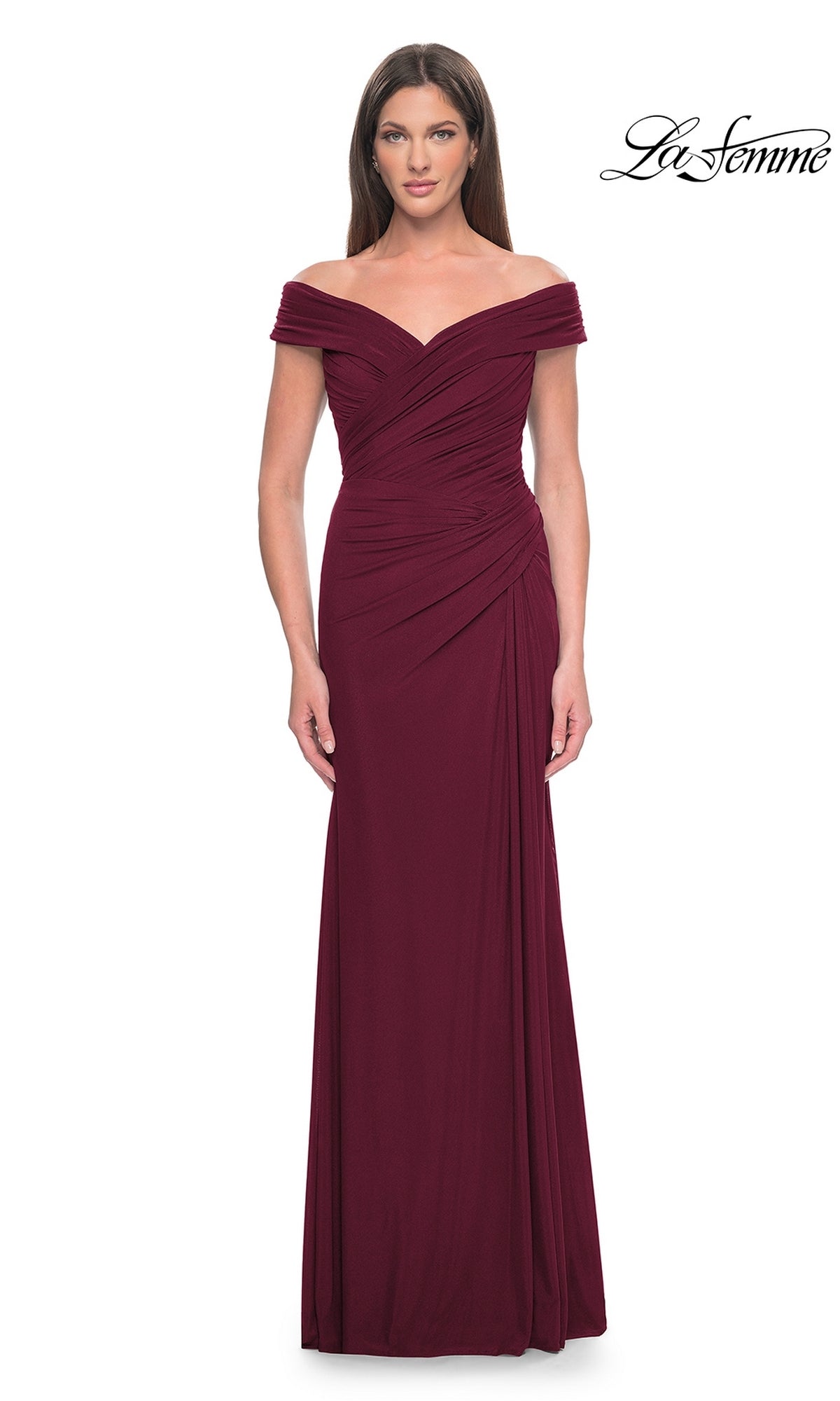 A woman wears the La Femme Off-the-Shoulder Long Prom Dress 31677 in burgundy, featuring ruched detailing and a fitted silhouette, standing against a plain white background for a classic formal look.